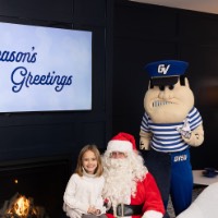 Little girl in white sweater and brown pants sits on Santa's lap